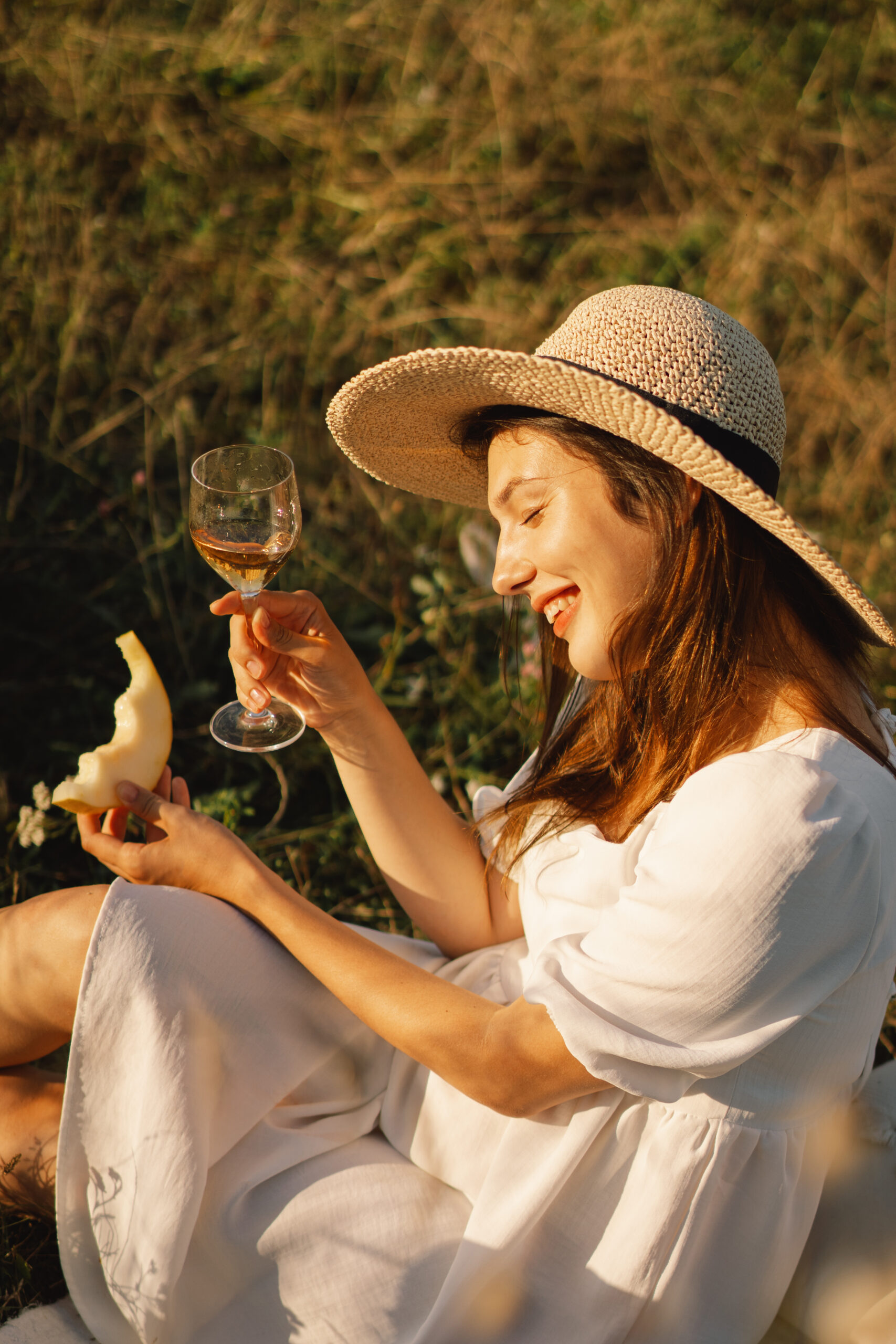 Young beautiful girl in a white dress having a picnic with a glass of champagne or white wine Young beautiful girl in a white dress having a picnic with a glass of champagne or white wine. Romantic picnic. Happy beautiful girl on the nature picnic. Summer time